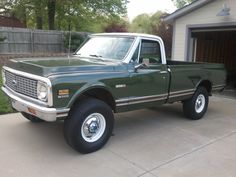 a green pick up truck parked in front of a garage