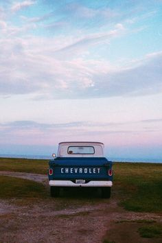 an old chevy truck parked on the side of a dirt road next to a grassy field