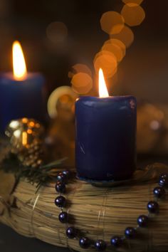 two lit candles sitting on top of a wooden table next to beads and pine cones