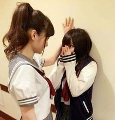 two young women standing next to each other in front of a wall holding their hands together