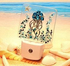 This LED Sensor Nightlight showcases an elegant three-dimensional jelly fish figure adorned with rhinestone accents and teal-colored gemstones. Its design is highlighted by a background of tiny glass fragments in aqua and silver along with a silver starfish. All elements are securely set in epoxy resin. This unique nightlight is the exact one that you will receive, available for prompt shipment. The sensor is automated, activating at dusk and deactivating at dawn with a warm white light. This eco-friendly LED sensor light consumes minimal electricity, and the bulb never requires replacement. The dimensions are 4.5 inches in height and 3 inches in width. It's versatile for use throughout your home, ideal for bedrooms, bathrooms, and hallways, or as a decorative coastal accent light to enjoy Unique Resin Ideas, Nightlight Ideas, Florida Coastal Decor, Accent Bathroom, Bathroom Night Light, Epoxy Projects, Accent Light, Sensor Light, Fused Glass Ideas