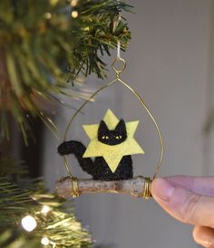 a hand holding a christmas ornament with a black cat on it's back