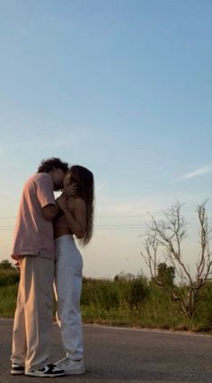 a man and woman kissing on the road in front of a kite flying high up in the sky