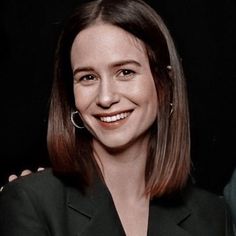 a smiling woman in a black suit and hoop earrings