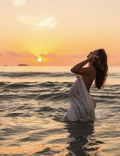 a woman standing in the ocean at sunset with her hands on her head and eyes closed