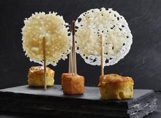 three small food items on top of a black plate with sticks sticking out of them