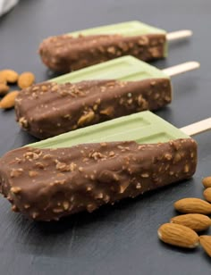 three popsicles with almonds and chocolate on them sitting on a black surface next to nuts