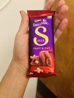 a person holding up a bar of dairy milk and fruit nut chocolate in their hand