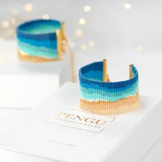 two bracelets sitting on top of a white box with blue and gold strips around it