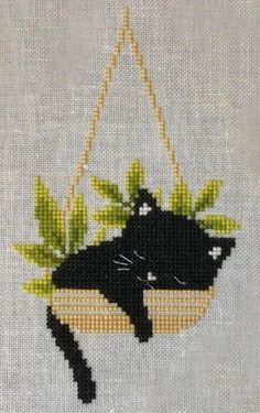 a black cat is sitting on a swing with green leaves hanging from it's back