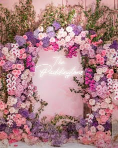 the wedding sign is surrounded by flowers and greenery in front of a pink backdrop