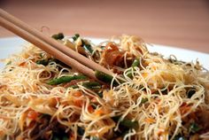 a white plate topped with noodles and veggies next to wooden chopsticks