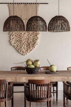 a wooden table topped with green apples under three hanging baskets filled with fruit on top of it