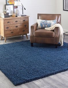 a living room with a chair, dresser and blue rug on the floor in front of it