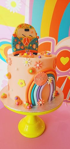 there is a colorful cake with flowers and rainbows on the top, sitting on a yellow pedestal