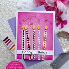 a birthday card with candles on it and pink flowers in the background, next to a spoon