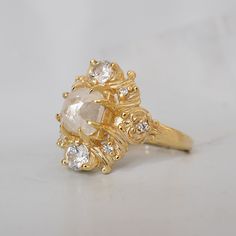 a gold ring with an oval shaped stone surrounded by smaller round cut diamonds on top