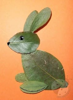 a green stuffed animal sitting on top of a leaf covered floor next to an orange wall