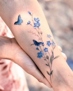 two people holding hands with blue flowers and butterflies tattooed on their arms, one has a butterfly tattoo on it's left arm