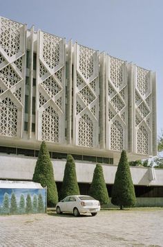 a white car parked in front of a building with intricately designed panels on it's side