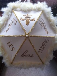 an umbrella that has been decorated with gold writing and white fur around the edges, on top of a chair