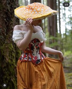 a woman in an orange and white corset is walking through the woods with a yellow hat on her head