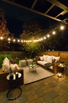 an outdoor living area with couches, tables and lights on the patio at night