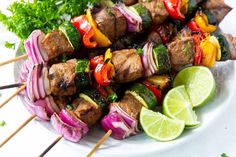 skewered meat and vegetables on a plate with lime wedges next to it