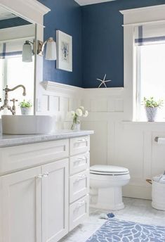 a bathroom with blue walls and white cabinets is pictured in this image, there are flowers on the counter next to the toilet