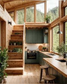 a kitchen with green cabinets and wooden steps leading up to the upper floor, along with potted plants