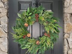 a wreath with pine cones and greenery hangs on a black door frame in front of a stone wall