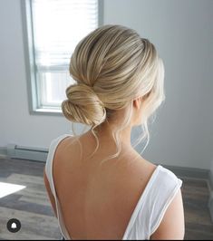 a woman with blonde hair in a white top is looking out the window and has her back to the camera