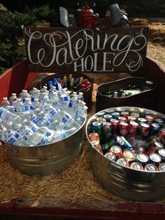 two metal buckets filled with water and soda bottles sitting on top of hay next to a sign