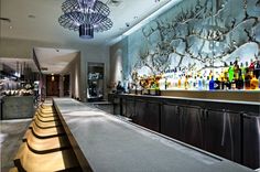 the bar is lined with liquor bottles and wooden stools in front of an artistic wall