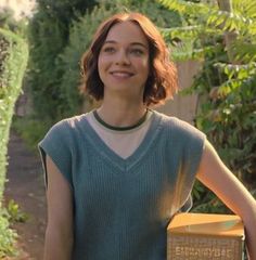 a woman standing in front of a garden holding a box with plants growing on it