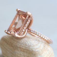 This Diamond Prong Morganite Ring is part of our Olivia Collection, which is characterized by a gorgeous, genuine gemstone with Golden Hearts under it. Diamonds stud the hidden halo and sparkle down the half eternity shank.  Custom initials at the back of the shank are available on all rings upon request!

Center Stone: Genuine AAA Peachy Pink Morganite, Emerald Cut, averaging 15x12mm and 10 carats.
Side Stones: 68 Diamonds – you choose Lab Grown or Organic – averaging F-G, VS2-SI1 and 0.46 cara Luxury Morganite Diamond Ring With Halo Setting, Luxury Morganite Ring With Prong Setting, Formal Morganite Ring With Halo Setting, Radiant Cut Gemstone Halo Ring, Morganite Diamond Ring With Accent Stones, Emerald Cut Rose Gold Halo Jewelry, Radiant Cut Diamond Ring With Gemstone, Emerald Cut Rose Gold Jewelry With Halo Design, Morganite Rings With Halo Design For Formal Occasions