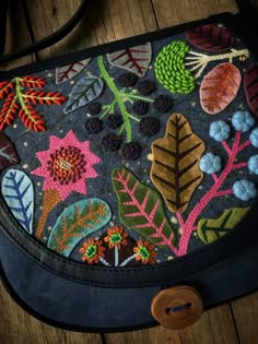 a handbag with embroidered leaves and flowers on the front, sitting on a wooden surface