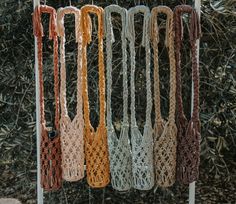 several crocheted bags hanging from a clothes line in front of bushes and shrubbery