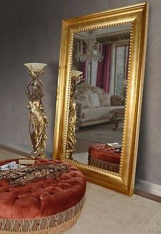 a large mirror sitting on top of a floor next to a foot stool and table