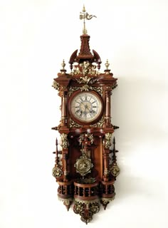 an ornate wooden clock is hanging on the wall in front of a white background with gold trimmings