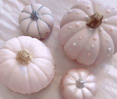 three white pumpkins with pearls on them are sitting on a bed and one has a gold brooch