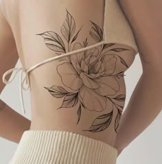 a woman's back with a flower tattoo on her left side ribcage