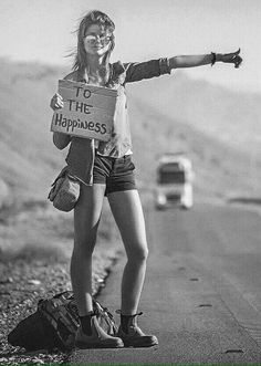 a woman standing on the side of a road holding a sign that says the happiness