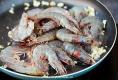 shrimp being cooked in a frying pan with garlic and seasonings on the side