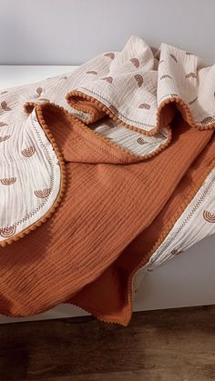 an orange and white blanket sitting on top of a bed next to a wooden floor