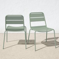 two green chairs sitting next to each other in front of a white wall and cement floor