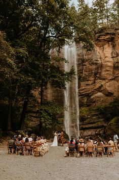 a group of people sitting at tables in front of a waterfall with a bride and groom