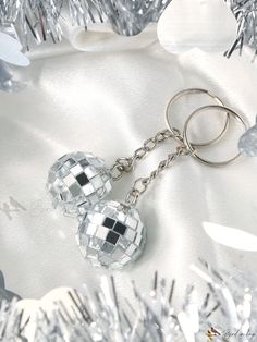 two mirrored disco ball keychains sitting on top of silver tinsel