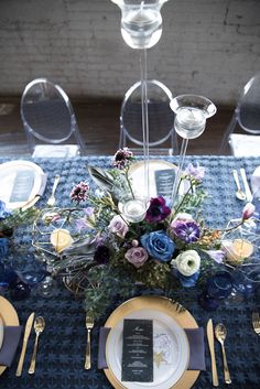 the table is set with plates, silverware and purple flowers on it's centerpiece