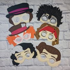 four masks with different faces are hanging on a brick wall in front of a white brick wall